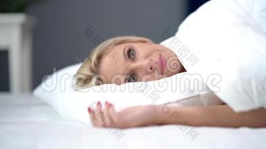 有问题的成年妇女在家中睡在白色羽绒被下